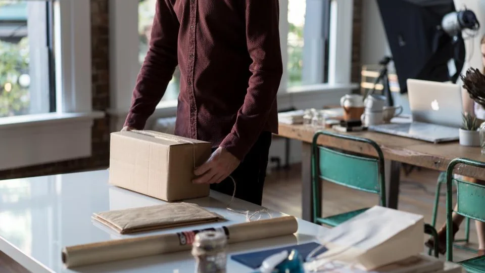 A pair of hands packing a small cardboard box at a desk