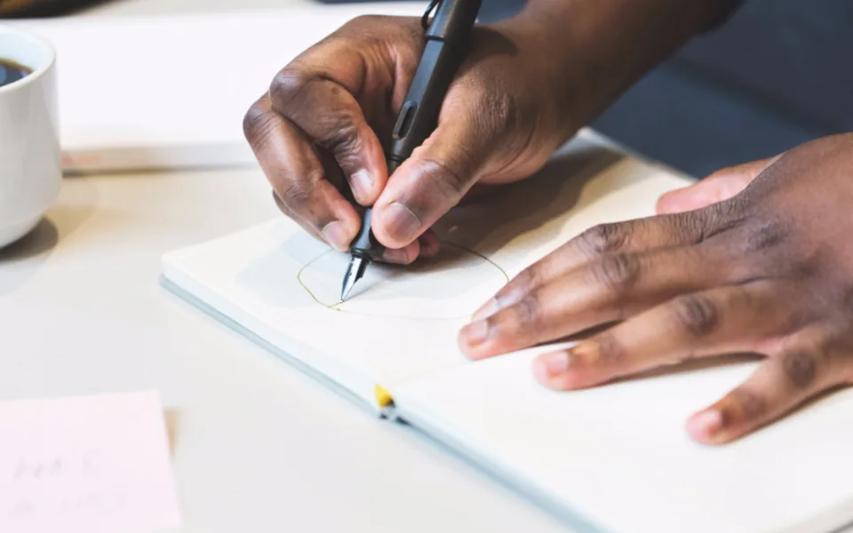 Hands drawing a curve in a notebook with a fountain pen, one hand steadying the page