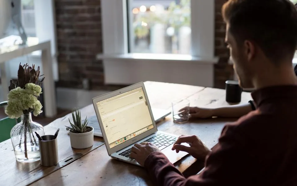 A person working at a laptop at a tidy desk beside a sunlit window