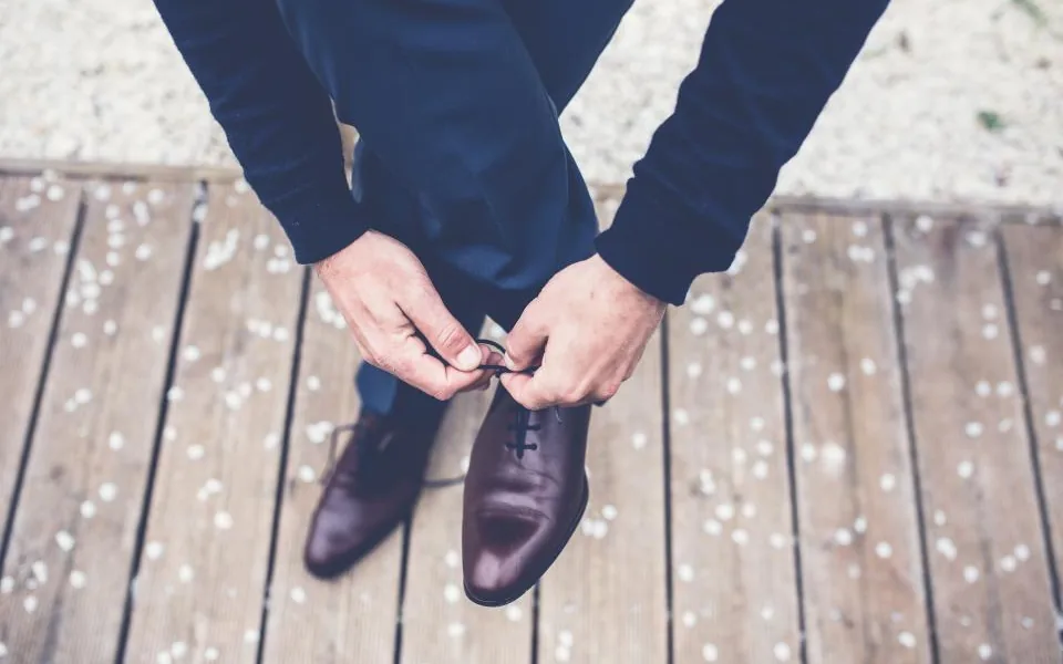 A person bending to tie their shoelaces, both hands on the laces
