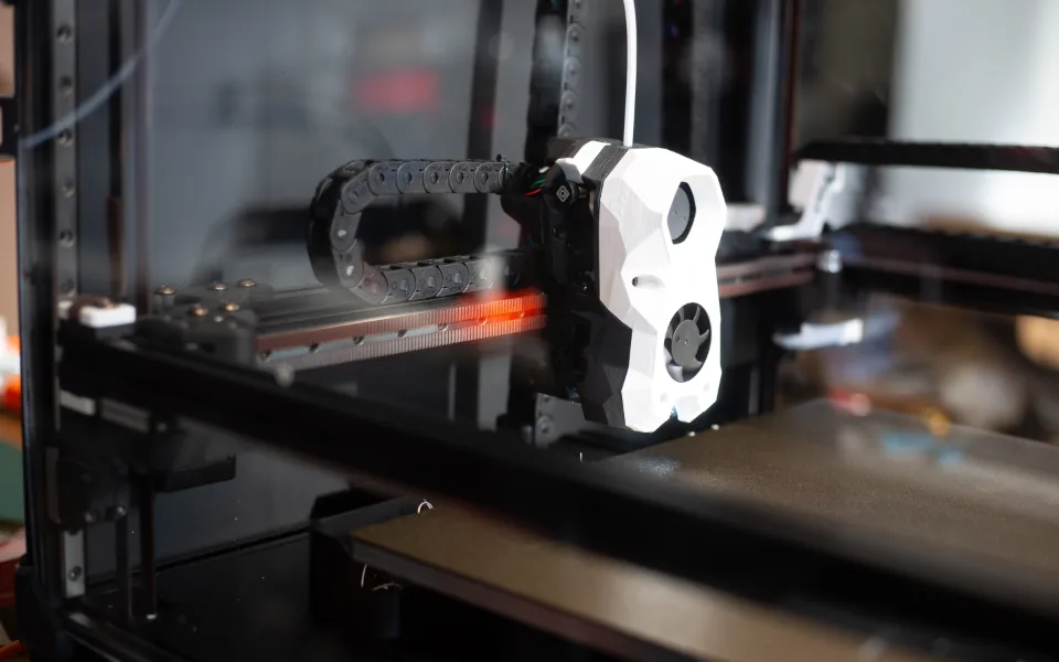 The printhead of an additive manufacturing machine moving on its gantry above the build plate