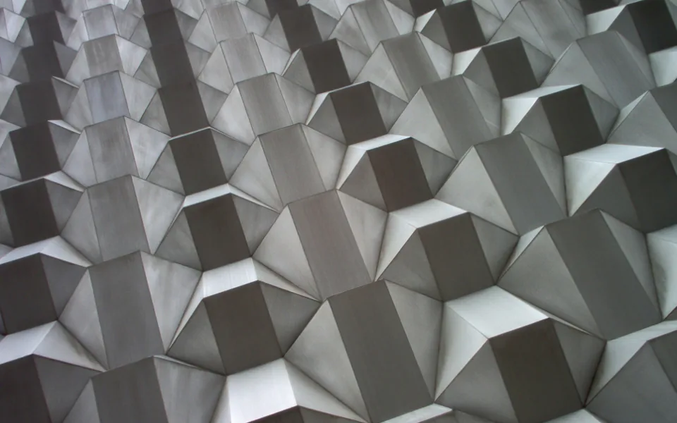 A pale wall of repeating three-dimensional facets, lit from one side