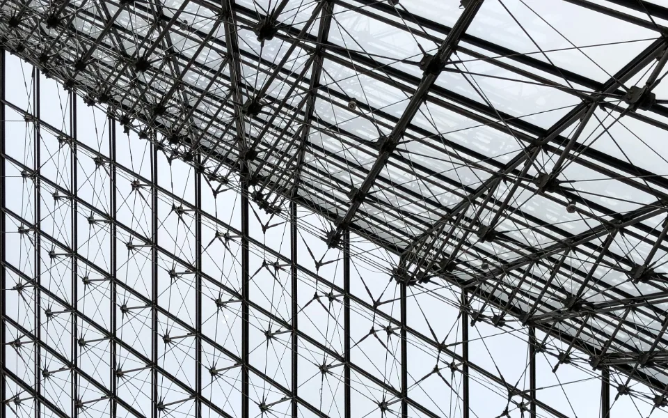 A glazed atrium wall and roof seen from below, its steel cable grid dividing the glass into a fine lattice