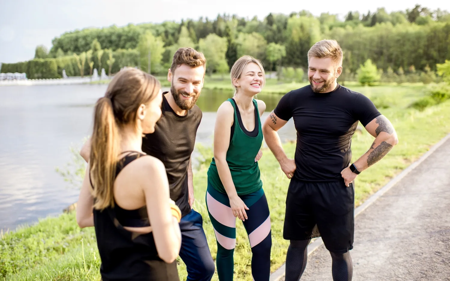 Four people in athletic wear standing together on a path beside a lake
