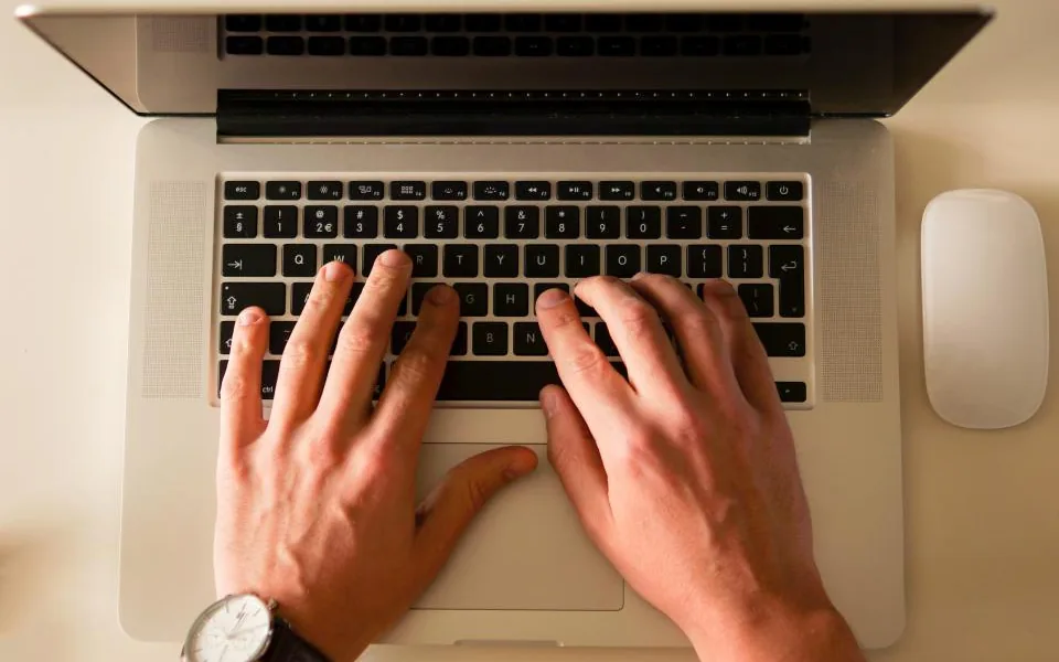 Hands resting on a laptop keyboard, photographed from directly above